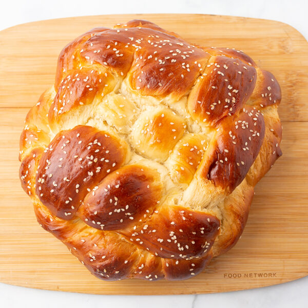 Image overlooking a warm golden brown challah bread on a cutting board.