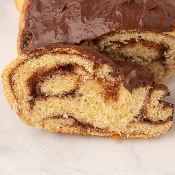 Image of a slice of warm chocolate swirled roll of babka bread with a chocolate glaze on the top