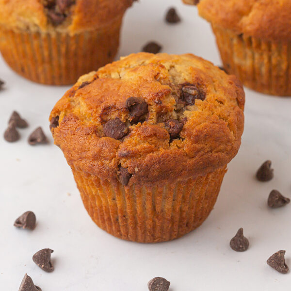 Image closeup of 3 banana chocolate chip muffins on a table decorated with chocolate chips.
