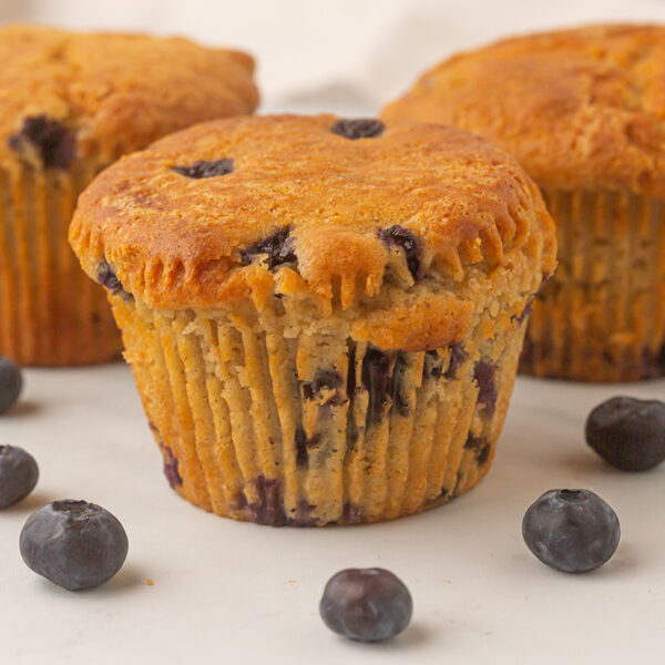 Image closeup of 3 blueberry muffins on a table decorated with blueberries.