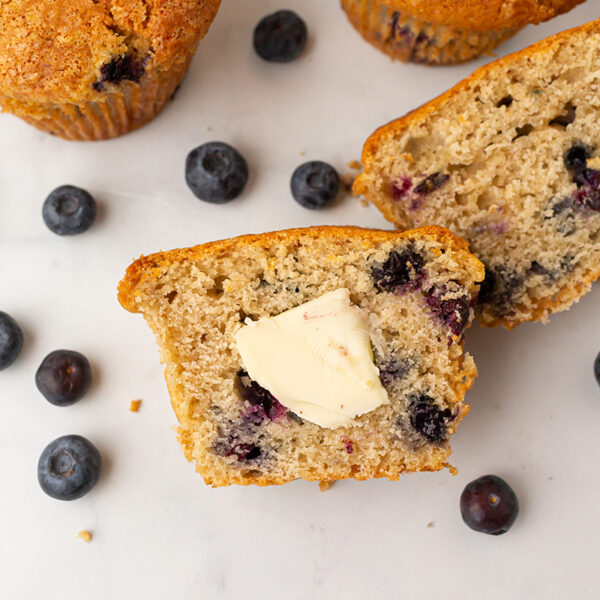A platter of warm fresh blueberry muffins sliced in half toped with Kerry gold Irish butter and garnished with fresh blueberries.