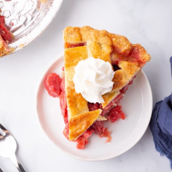 A fresh slice of Strawberry Rhubarb pie with whipped cream on top
