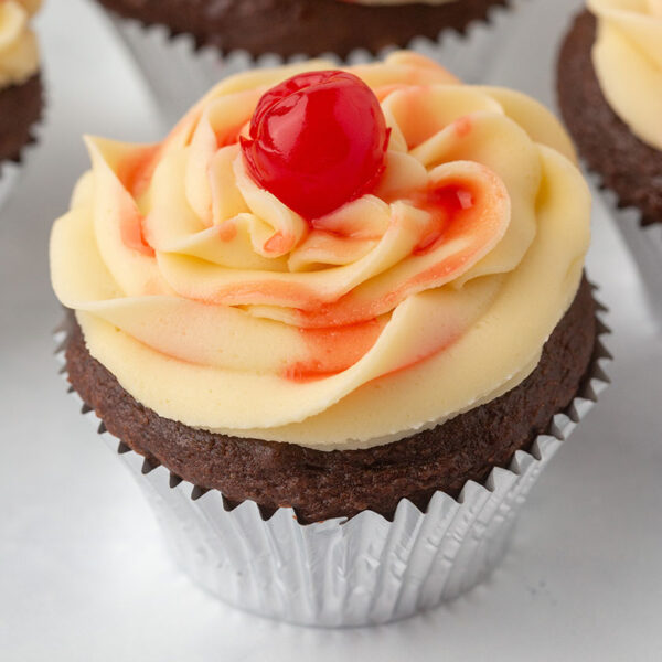 chocolate cupcake with vanilla icing topped with maraschino cherries