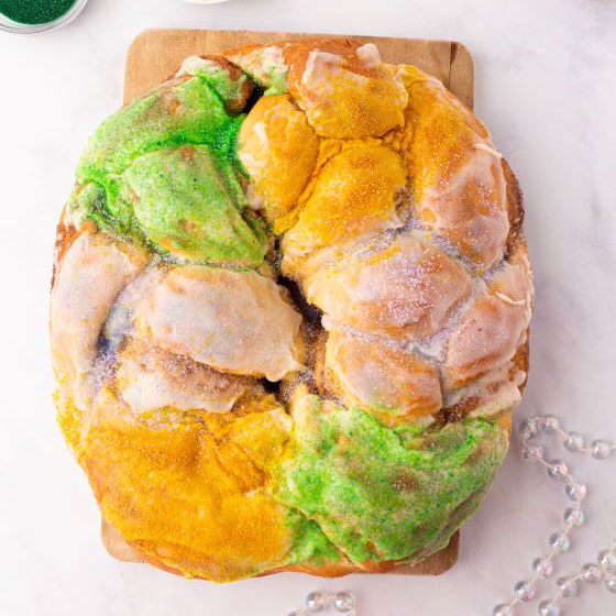 Whole Mardi Gras King cake, a mixture of coffee and a cinnamon roll iced and topped with traditional Mardi Gras colors of purple, green, and gold.