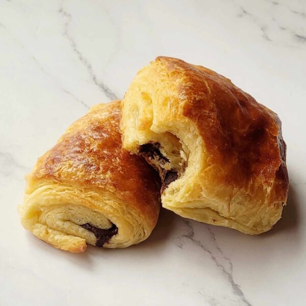 Two croissants one sitting atop another both with gooey chocolate oozing out of the middle.