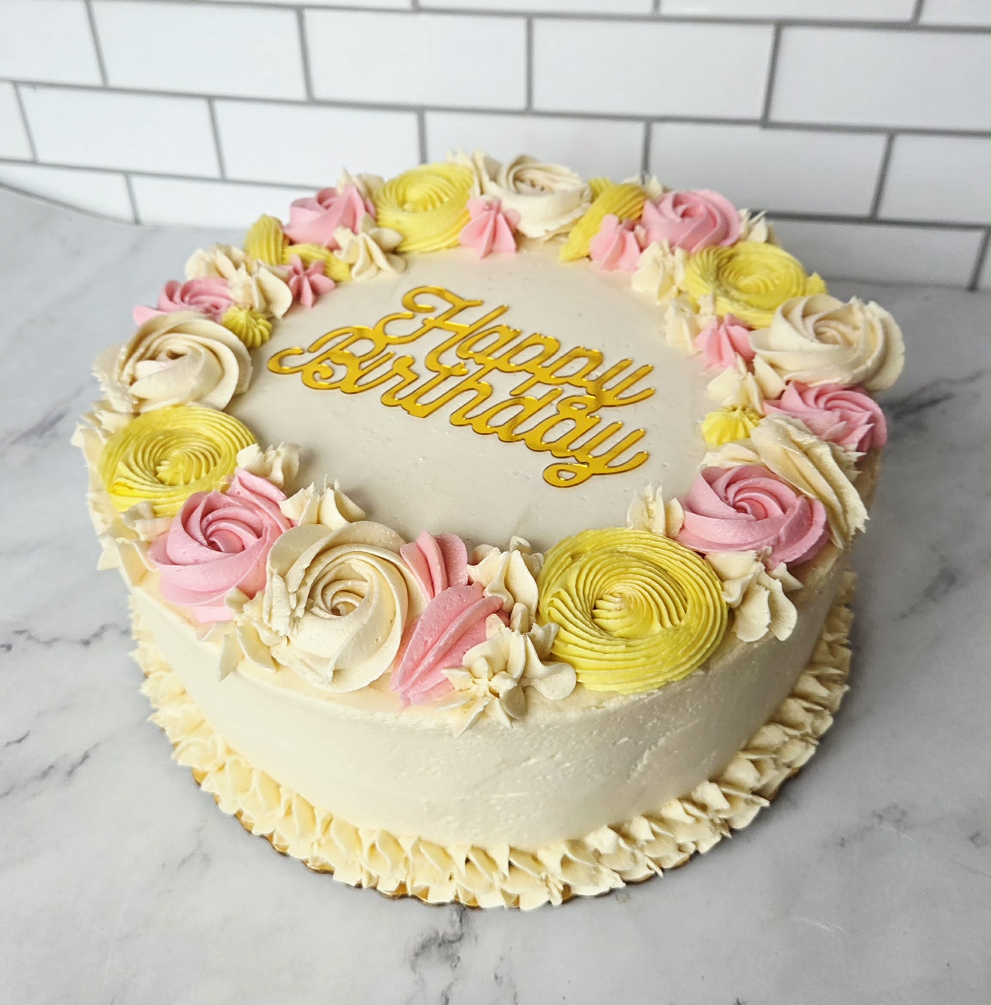 Pastel Easter buttercream cake with pink, yellow, and ivory floral piping and Happy Birthday message, available for spring holiday dessert ordering.